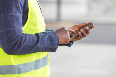 Mobil uygulama kullanan bir mühendis. Mühendis, mimar ya da yönetici yeni bir ofis binasının önünde, planları tutuyor ve mobil bir uygulama kullanıyor. Foreman talimatları akıllı telefondan gönderiyor