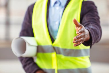 Koruyucu miğfer ve yelek giyen yakışıklı inşaat işçisi elini sıkmak için uzatıyor. El sıkışmaya hazır bir mimar - anlaşma, ortaklık ve kazan-kazan durumu konsepti