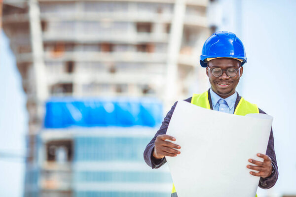 Portrait of construction inspector posing with blueprints on building site. Portrait of handsome foreman construction worker on a industrial building industry construction site