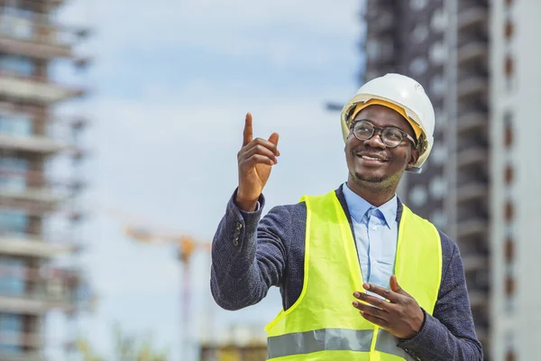 Construction worker at building site smiling at camera. Portrait of mature engineer in a construction site looking at camera. Successful african architect wearing helmet and uniform with copy space.