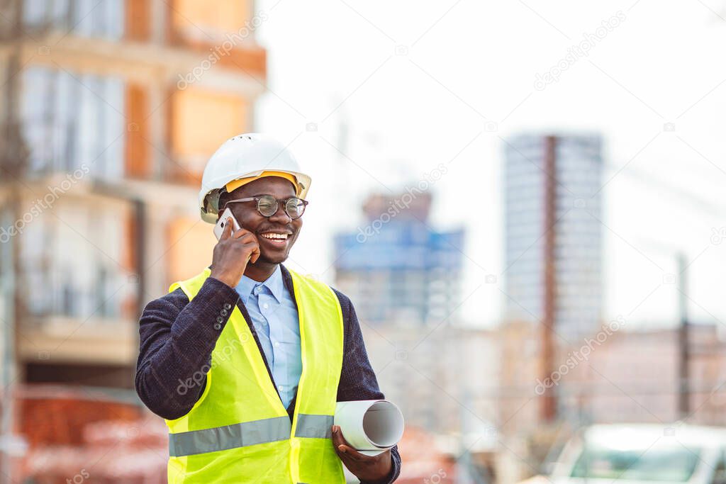 Confident construction manager wearing hardhat and talking with smarphone. Successful mature civil engineer at construction site with copy space. Engineer portrait in a site plant