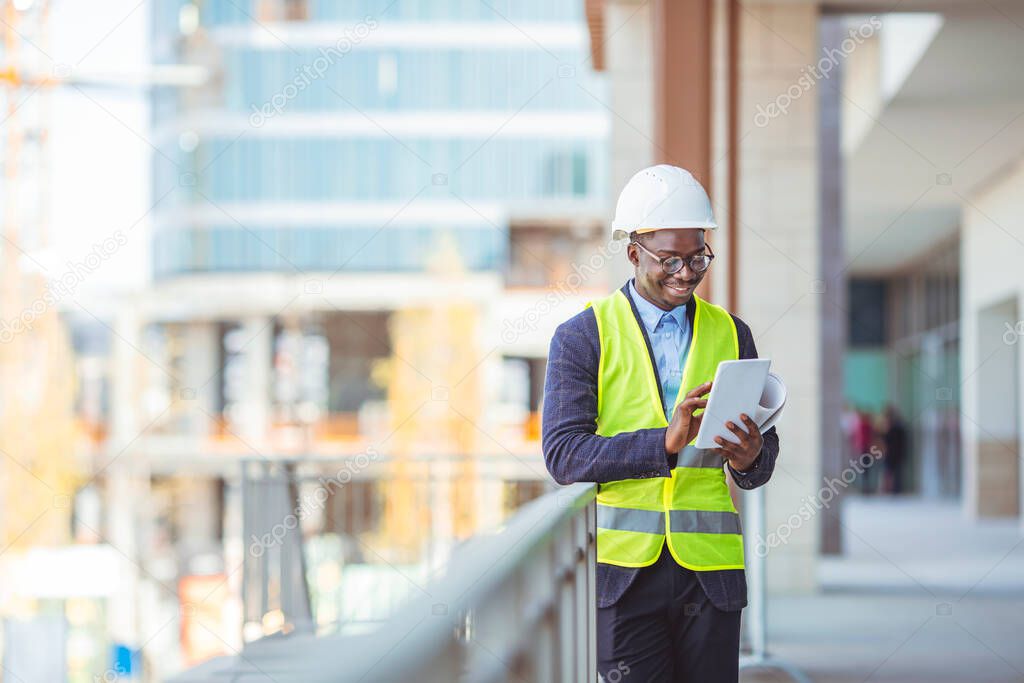 Portrait of smiling Engineer / Architect looking at camera. Working on a new office building. Happy mid adult engineer. Man engineer walking on construction site, holding tablet.