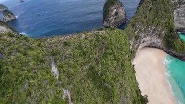 Nusa Penida, Bali 'deki Kelingking Sahili' nin üzerinde uçan FPV insansız hava aracı görüntüleri turkuaz suyu ve beyaz kumları gösteriyor..