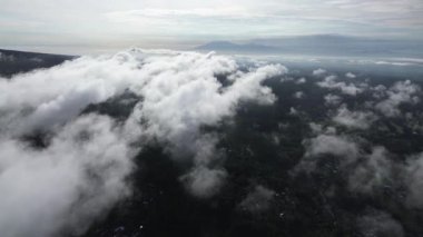 Endonezya 'da açık mavi bir gökyüzü altında alçak bulutlar ve uzak volkanla tropikal ormanın hava aracı görüntüsü