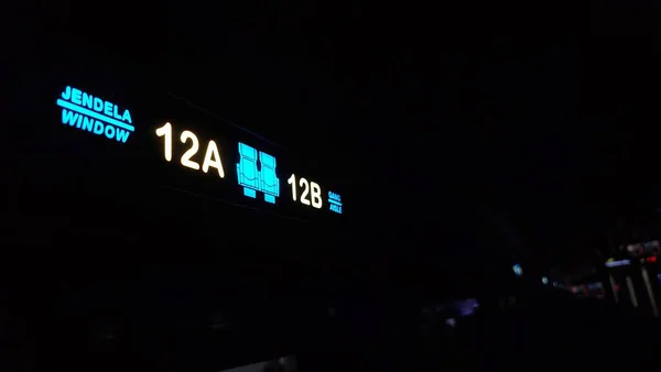 Aydınlatılmış koltuk numarası işareti, 12A ve 12B koltukların koyu renkli kabin ortamında parlak simgeler ve iki dilli etiketlerle gösterildiğini gösteriyor.