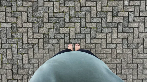 İnsan bakış açısı, yıpranmış yüzeyi olan, birbirine kenetlenmiş gri tuğla kaldırım dokusuna bakıyor.