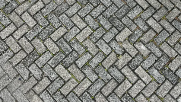 Yıpranmış yüzeyi olan gri iç içe geçmiş tuğla kaldırım dokusu, arka plan, inşaat, kentsel ve tasarım uygulamaları için ideal.