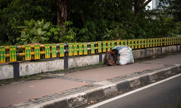 Zavallı adam kaldırım kenarındaki bir poşet plastik çöp kutusunda uyuyor.