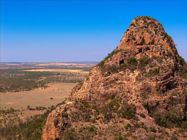 A stunning aerial drone view captures the rugged mountain ranges of Outback Queensland, Australia, revealing the raw beauty of a remote wilderness landscape. The scene showcases rocky ridgeline, dramatic terrain, horizons stretching into the distance