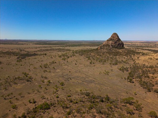 A stunning aerial drone view captures the rugged mountain ranges of Outback Queensland, Australia, revealing the raw beauty of a remote wilderness landscape. The scene showcases rocky ridgeline, dramatic terrain, horizons stretching into the distance