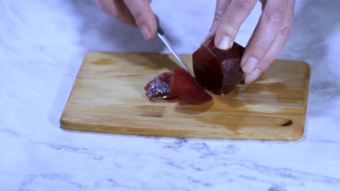 Ahşap kesme tahtasında haşlanmış pancar dilimleyen kadın elleri keskin bir mutfak bıçağıyla ahşap bir tahtanın üzerinde yumuşak, koyu kırmızı bir pancar dilimliyor. Canlı sebzenin sağlıklı bir salata için hazırlanışının detaylı görüntüsü.