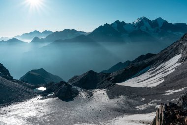 Güneşin altında yüksek irtifada bir buzul manzarası, dağların zirveleri sisli bir vadiye dönüşüyor..