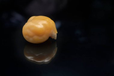 Nohutun canlı turuncu-bej rengi koyu siyah arkaplanla çelişiyor. Kremsi dokusunu ve beyin kıvrımlarına benzeyen girintileri vurguluyor..