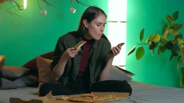 Evdeki kanepede oturan ve pizza yiyen bir kadın. akıllı telefon