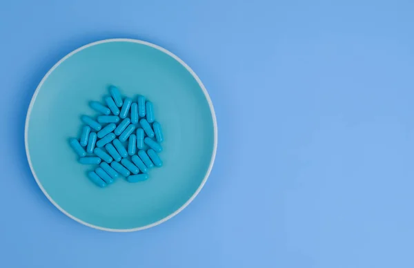 Pastillas azules en un plato de color sobre un fondo azul. Fotos de stock libres de derechos