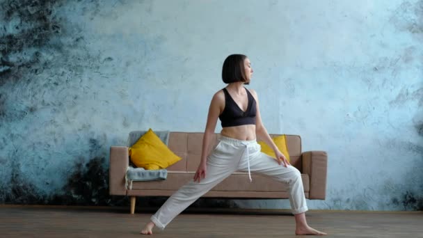 Wanita di ruang tamunya dalam pose yoga prajurit. — Stok Video