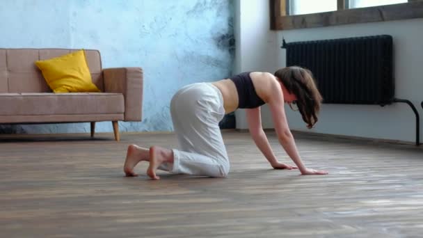 Schattige brunette vrouw doet yoga oefeningen in modern huis op de bank achtergrond. — Stockvideo