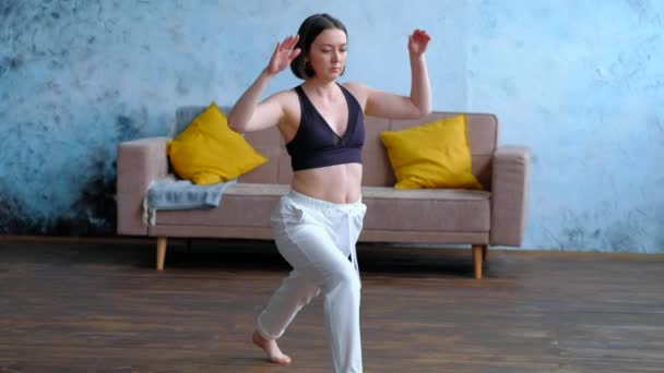 Vrouw in haar woonkamer in krijger yoga pose. — Stockvideo