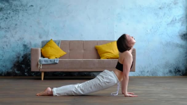 Linda mujer morena hace ejercicios de yoga en casa moderna en el fondo del sofá. — Vídeos de Stock