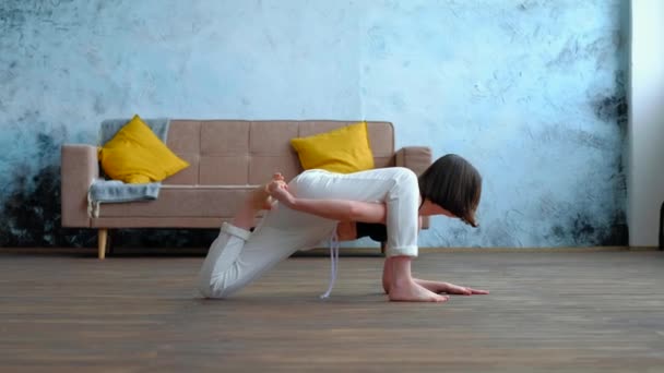 Schattige brunette vrouw doet yoga oefeningen in modern huis op de bank achtergrond. — Stockvideo