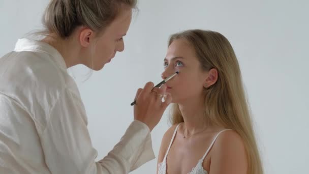 Jonge make-up kunstenaar doet make-over naar mooi model — Stockvideo
