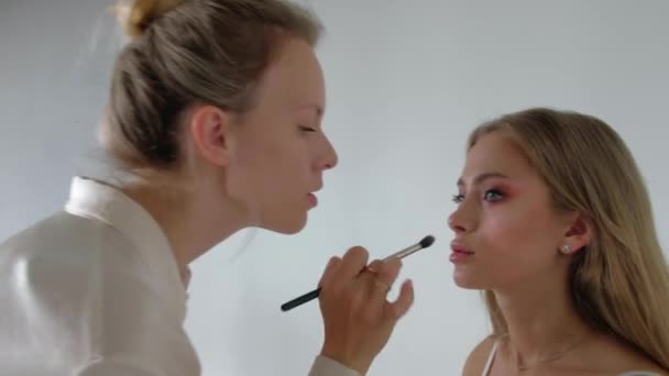 Jonge make-up kunstenaar doet make-over naar mooi model — Stockvideo