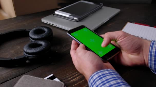 Ruce člověka pomocí smartphonu se zelenou obrazovkou na dřevěném stole. — Stock video