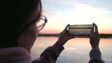 Arka plandaki kadın yaz günü gün batımının telefonuyla fotoğraf çekiyor..