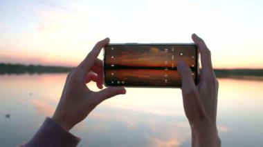 Yaz günü gün batımının telefonuyla fotoğraf çeken bir kadının elleri.