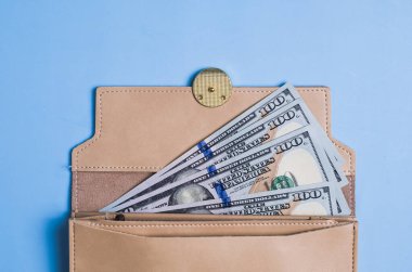 Mavi arka planda 100 dolarlık banknotlar ve cüzdan.