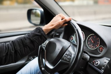 Bir adam modern siyah deri kaplamalı bir araba kullanıyor. Pencerenin dışında bir sonbahar şehri görülebilir.