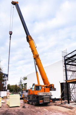 İnşaat alanında çalışan bir kamyon vinci. Bölge çitlerle çevrili ve yeni bir yapı inşa ediliyor. Yakınlarda bir ayak kaldırma yeri görünüyor..