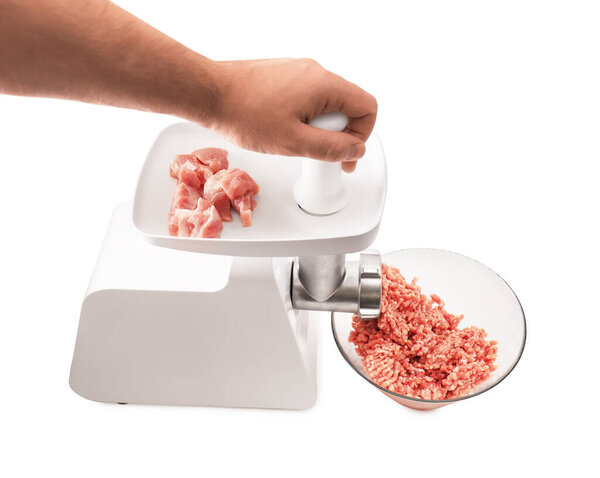 Белая электрическая мясорубка с белым пластиковым плунжером, отбивающая куски сырой свинины в прозрачную стеклянную миску на белом. Высокое качество фото
