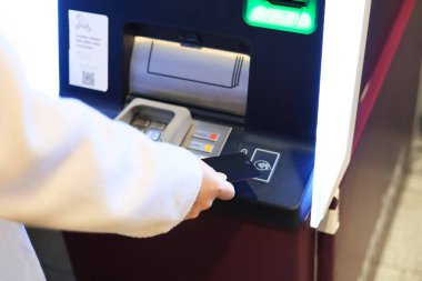Modern bir ATM makinesinin tarayıcısının yanında para transferi için siyah bir banka kartı tutan bir kişi. Yüksek kalite fotoğraf