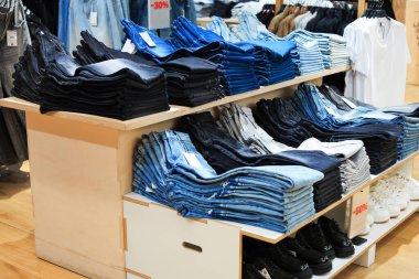 Katlanmış mavi, siyah ve gri kot pantolon yığınları% 30 işaretli bir perakende giyim mağazasında ahşap raflarda sergileniyor. Yüksek kalite fotoğraf