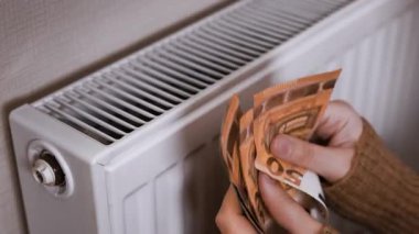 Avro banknotlarını (50 'likler ve 20' likler) sayan eller ve bunları yüksek ısıtma maliyetlerini sembolize ederek beyaz ısıtma radyatörüne yerleştirmek. Yüksek kalite 4k görüntü