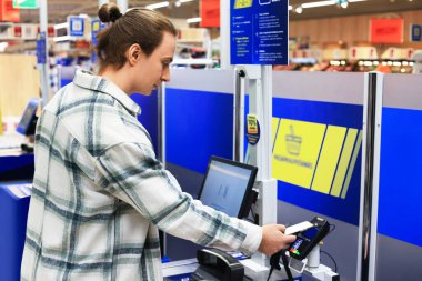 Bir adam, markette ya da süpermarkette modern self-servis terminalinde ödeme yapmak için akıllı telefon kullanıyor. Yüksek kalite fotoğraf