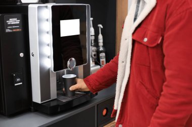 Kırmızı kadife ceketli genç adam, siyah bir fincana sıcak içecek koymak için modern, otomatik bir kahve makinesi kullanıyor. Yüksek kalite fotoğraf