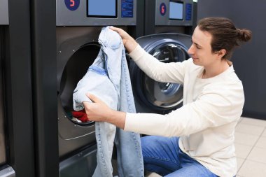 Adam çamaşırhanedeki çamaşır makinesine kot pantolon koyuyor. Yüksek kalite fotoğraf