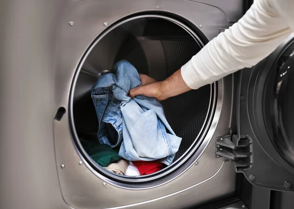 Bir adamın eli, kot pantolonları ve kıyafetleri modern bir çamaşır makinesine yüklerken yakın plan çekilmiş. Yüksek kalite fotoğraf