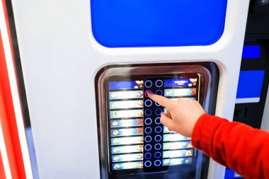 Kırmızı kazaklı bir kişi dokunmatik ekranlı, parlak ışıklı bir otomattan bir içecek seçer. Yüksek kalite fotoğraf