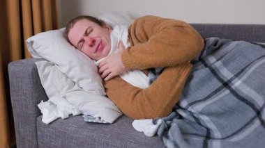 Hasta adam, grip salgını sırasında etrafı mendillerle çevrili kanepede yatarken acı içinde öksürüyor. Yüksek kalite 4k görüntü