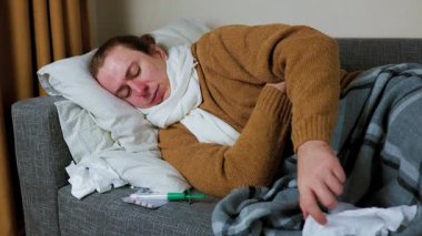 Hasta bir adam kanepede yatıyor, öksürüyor. Bir kadın onunla ilgileniyor ve ona nebulizör veriyor. Sağlık ve grip tedavisi kavramı. 4 bin. Yüksek kalite 4k görüntü