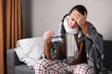 Battaniyeli hasta adam termometreyle ısıyı ölçüyor ve koltuğun alnına dokunuyor. Yüksek kalite fotoğraf