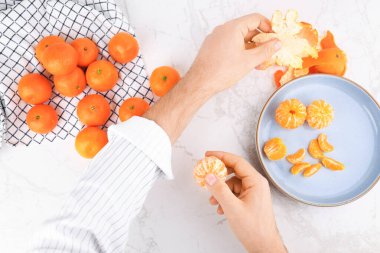 Beyaz mermer masada taze mandalina soyan erkek elleri. Sağlıklı narenciye yiyen bir adamın en iyi görüntüsü. Yüksek kalite fotoğraf