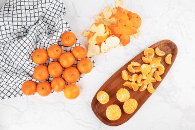 Taze mandalinalar, ahşap tabakta soyulmuş segmentler ve beyaz mermer masadaki deriler. Üst görünüm düz konum. Yüksek kalite fotoğraf