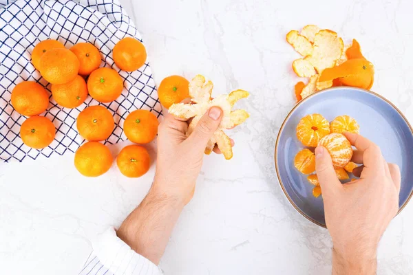 Erkek eller taze mandalinaları mavi plaka ve kareli havluyla beyaz mermer masada soyuyorlar. Üst görünüm düz konsept. Yüksek kalite fotoğraf