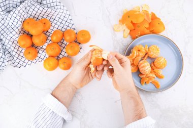 Beyaz mermer bir masa üzerinde taze mandalina soyan erkek ellerinin üst görüntüsü. Meyve ve tabağı dolu. Yüksek kalite fotoğraf