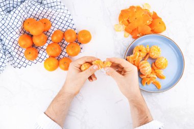 Mandalina segmentlerini taze meyve ve mavi tabakla beyaz mermer bir masada ayıran erkek ellerinin üst görüntüsü. Yüksek kalite fotoğraf
