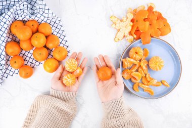 Kabuğu soyulmuş kadın elleri ve taze meyveli beyaz mermer bir masada mandalinaların üst görüntüsü. Yüksek kalite fotoğraf